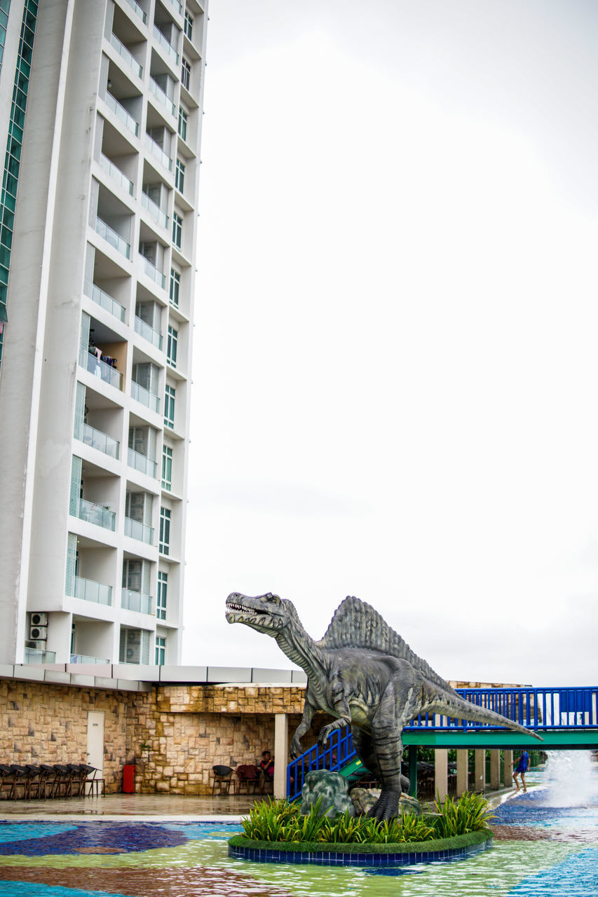 STATUE BY SWIMMING POOL IN CITY AGAINST SKY