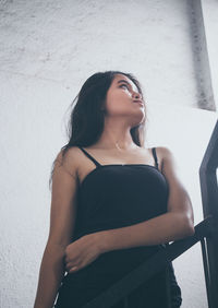 Low angle view of young woman looking away while standing against wall