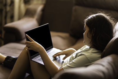 Chubby asian teen girl works on a laptop at home, sitting on sofa