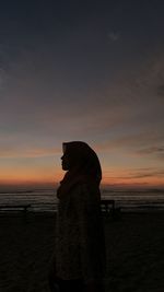 Silhouette woman standing on beach against sky during sunset