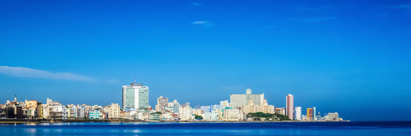 Sea by modern buildings against blue sky