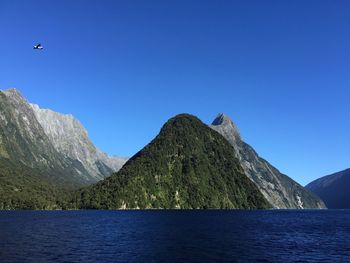 Scenic view of sea and mountains against clear blue sky