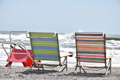 Empty chairs on beach against sky