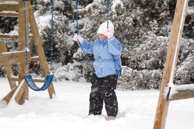 Boy playing on swing in playground during snowfall