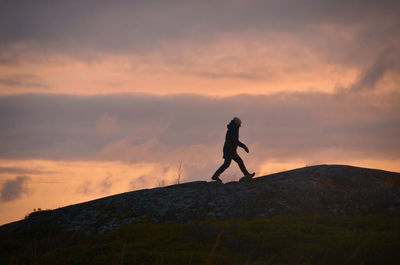 Woman walking on mountain against sky during sunset