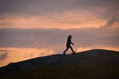 Silhouette person standing on rock against sky during sunset