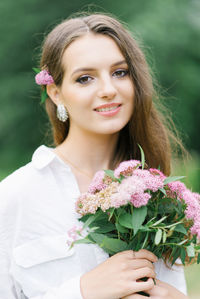 Outdoor close-up portrait of a beautiful young woman with pink flowers on a sunny day in the park