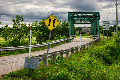 Information sign on road by bridge against sky