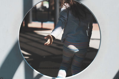 Rear view of girl gesturing seen through hole in play equipment