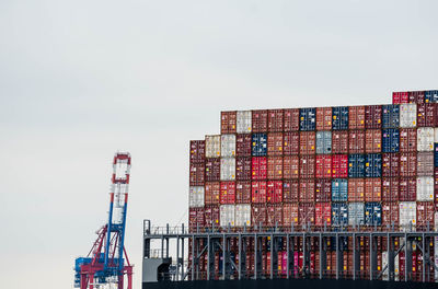 Low angle view of cranes and cargo containers against sky