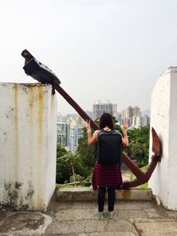 Rear view of woman showing victory sign while standing by rusty anchor on building terrace