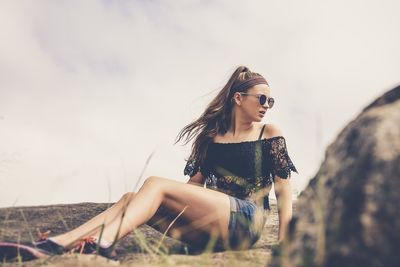 Young woman wearing sunglasses sitting on field against sky