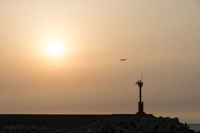 Mid distance view of silhouette lighthouse on pier during sunset at jeju island