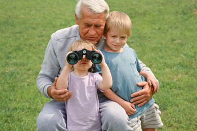 Side view of senior woman photographing while sitting on field