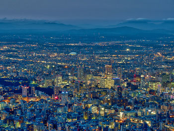 Aerial view of illuminated cityscape against blue sky