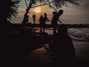 Silhouette people on beach against sky during sunset