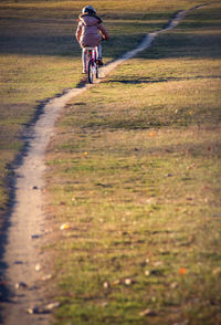 Rear view of girl riding bicycle on field