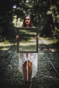 Portrait of woman holding mirror while standing on footpath