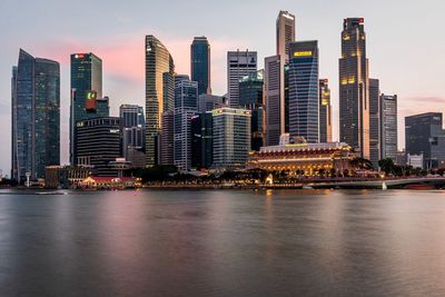 Illuminated buildings by river against sky in city