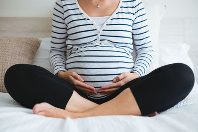 Midsection of woman sitting on bed at home