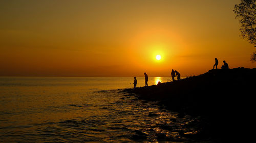 Silhouette people on beach against sky during sunset