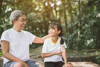 Grandfather sitting with granddaughter against trees