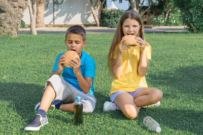 Children schoolchildren eat burgers in the park sitting on the grass. school lunch.