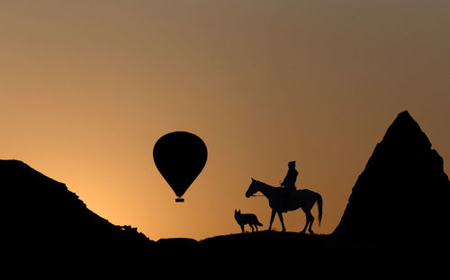 Silhouette person riding horse against orange sky