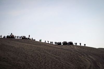 People on sand dune in desert against clear sky