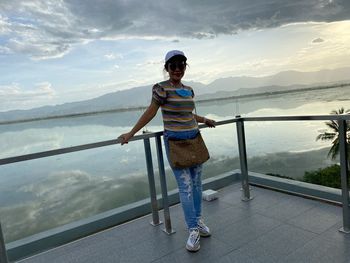 Portrait of woman standing on railing against sky