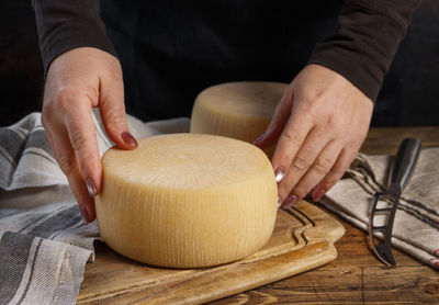 Somebody hands put a wheel of fresh homemade cheese on a wooden board close up