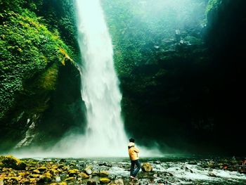 Man standing on rock against waterfall