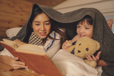 Mother and girl reading book while relaxing on bed