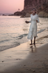 Beautiful african woman in sun hat walks on beach at sunset.
