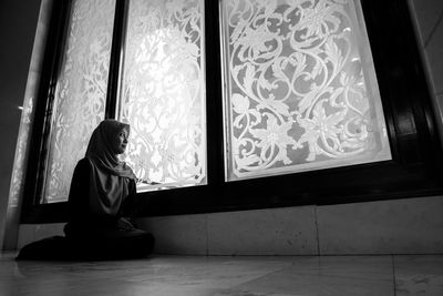 Side view of young woman looking through window at home