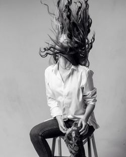 Woman with tousled hair sitting on stool against wall