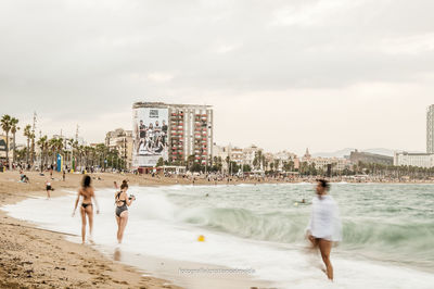 People on beach against sky in city