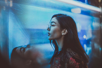 Close-up of young woman standing against illuminated city at night