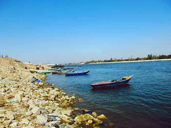 Boats moored in sea against clear blue sky