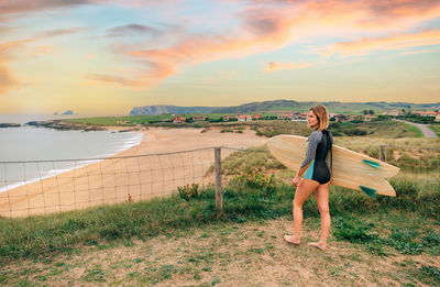 Surfer woman with wetsuit and surfboard looking at the beach