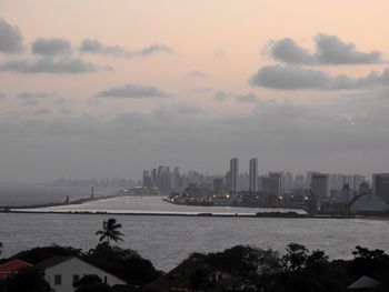 Sea by cityscape against sky during sunset