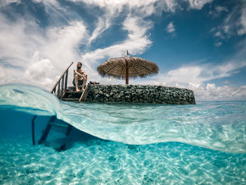 Low angle view of man sitting on rock in sea against sky