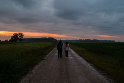 People walking on road against sky during sunset