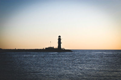Silhouette lighthouse by sea against clear sky during sunset