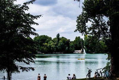 People in lake against cloudy sky