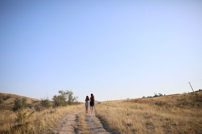 Rear view of people walking on field against clear sky