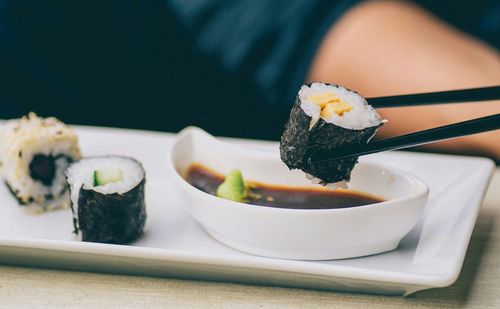 Cropped image of person holding sushi with chopsticks at restaurant table