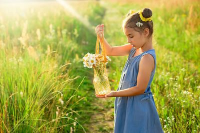 Cute little girl holding a knitted bag with a bouquet of daisies in a field