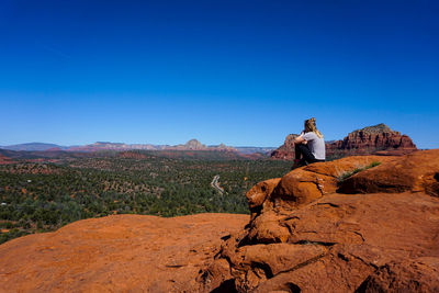 Teenage girl sitting on rock formation against clear sky