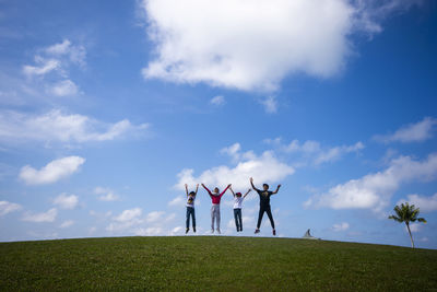 Low angle view of friends jumping on hill against blue sky